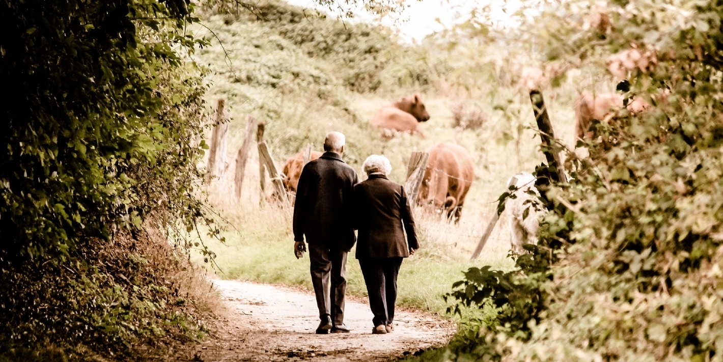 Two seniors walking down a path, holding hands