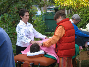Two people stand on either side of a person face down under a blanket, placing their hands on top