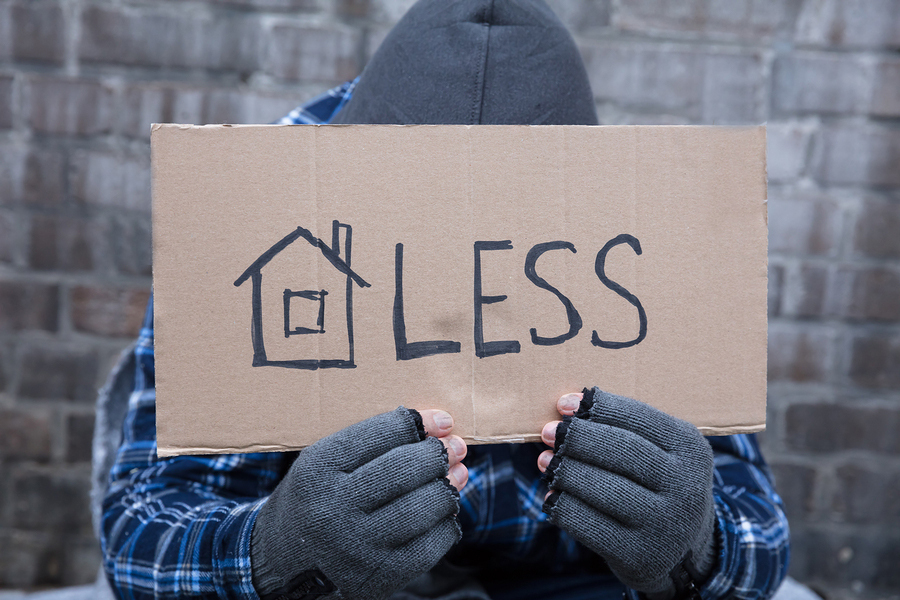 Person holding cardboard sign. cardboard sign has a simple drawing of a house followed by "less"