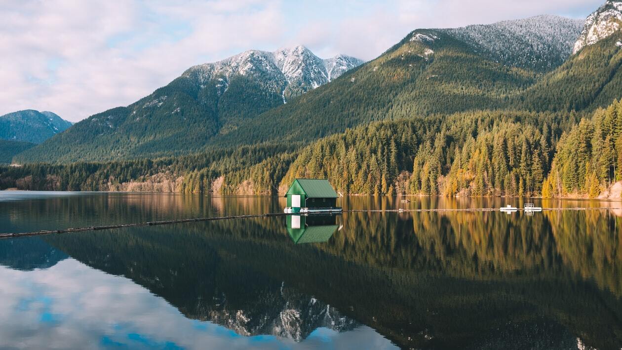 Small green cabin on the ocean water. Forests and mountains in the background.